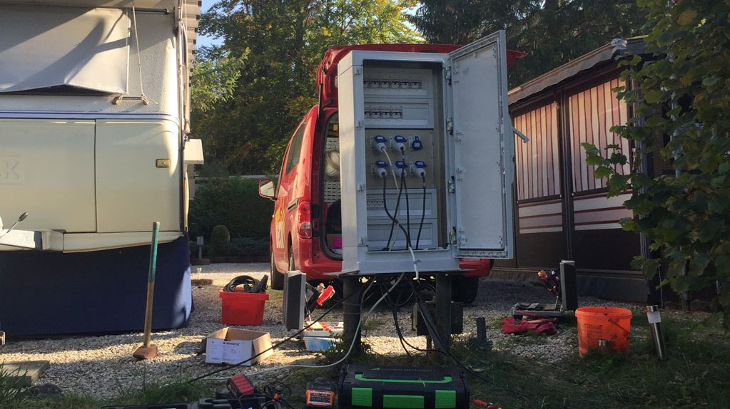 Fahrzeug von Elektro Beck hinter einem Verteilerkasten auf einem Camping-Platz, der gerade gewartet wird. Rings um den Kasten ist benötigtes Werkzeug zu sehen