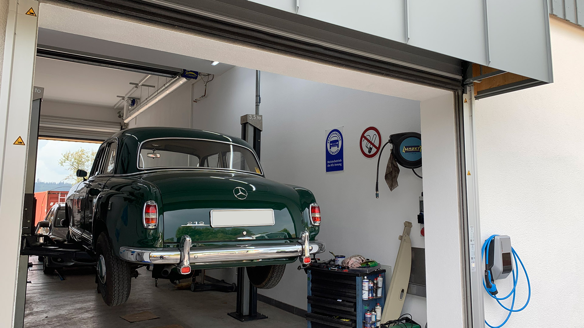 Ein grünes Auto befindet sich auf einer Hebebühne in einer KFZ Werkstatt